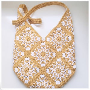 Puede incluir: Un bolso de hombro de crochet con un patr&oacute;n amarillo y blanco. El bolso tiene un cierre de bot&oacute;n &uacute;nico y una correa larga.
