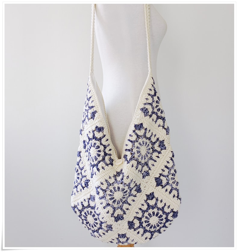 Puede incluir: Un bolso tote de crochet blanco con un patr&oacute;n floral azul. El bolso tiene una correa larga y est&aacute; hecho de un material suave y ligero.