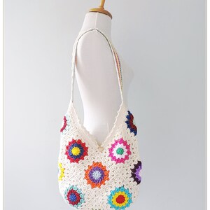 May include: A white crocheted tote bag with colorful granny square motifs. The bag has a long strap and is perfect for carrying everyday essentials.