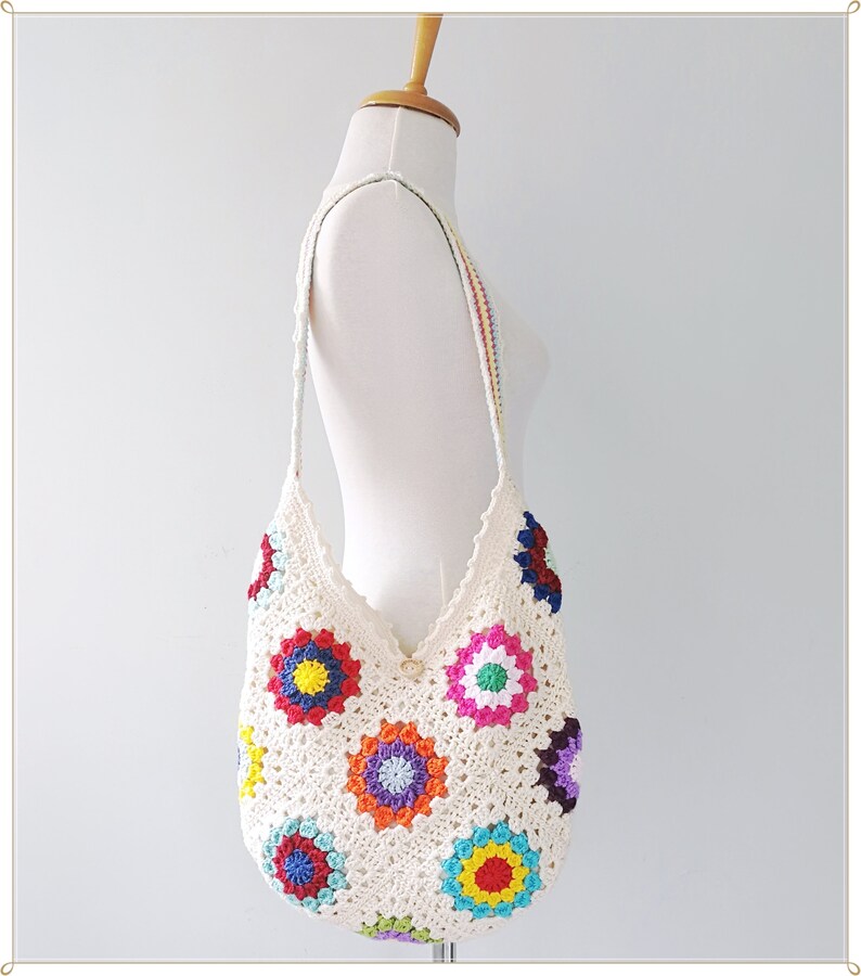 May include: A white crocheted tote bag with colorful granny square motifs. The bag has a long strap and is perfect for carrying everyday essentials.