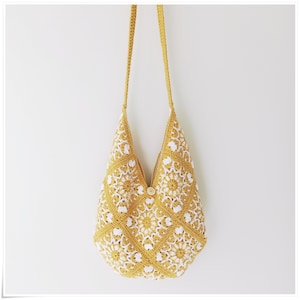 Puede incluir: Un bolso de hombro de crochet amarillo con detalles florales blancos. El bolso tiene una correa larga y un cierre de bot&oacute;n.