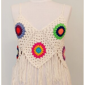 Puede incluir: Top blanco de crochet con detalles de flores de colores y ribete de flecos.