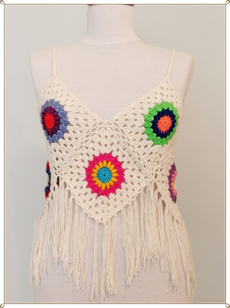 Puede incluir: Top blanco de crochet con detalles de flores de colores y ribete de flecos.