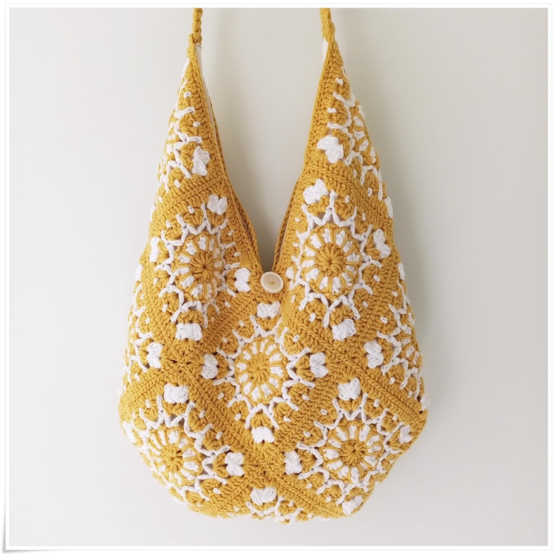 May include: A crocheted tote bag with a yellow and white geometric pattern. The bag has a single button closure.