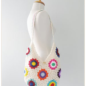 May include: A white crocheted tote bag with a colorful floral design. The bag has a long strap and is made with a granny square pattern.