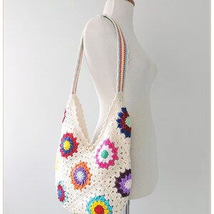 May include: A white crocheted tote bag with a colorful floral design. The bag has a long strap with stripes of red, yellow, and blue.