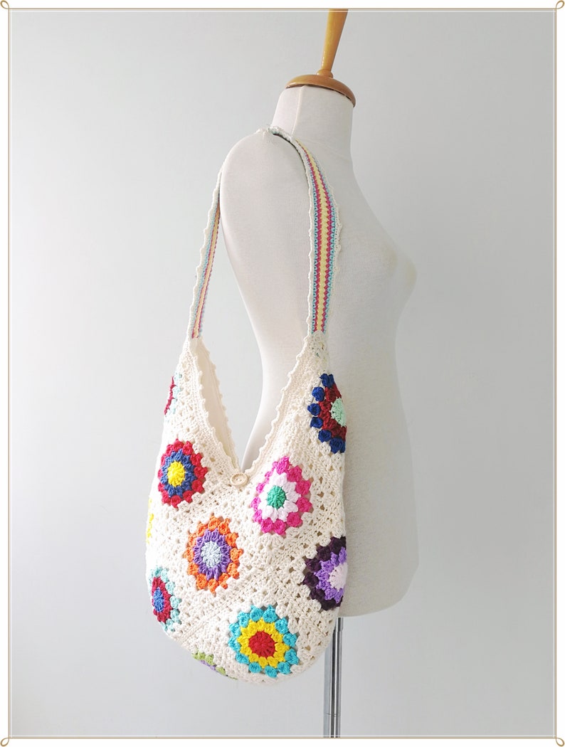 May include: A white crocheted tote bag with a colorful floral design. The bag has a long strap with stripes of red, yellow, and blue.