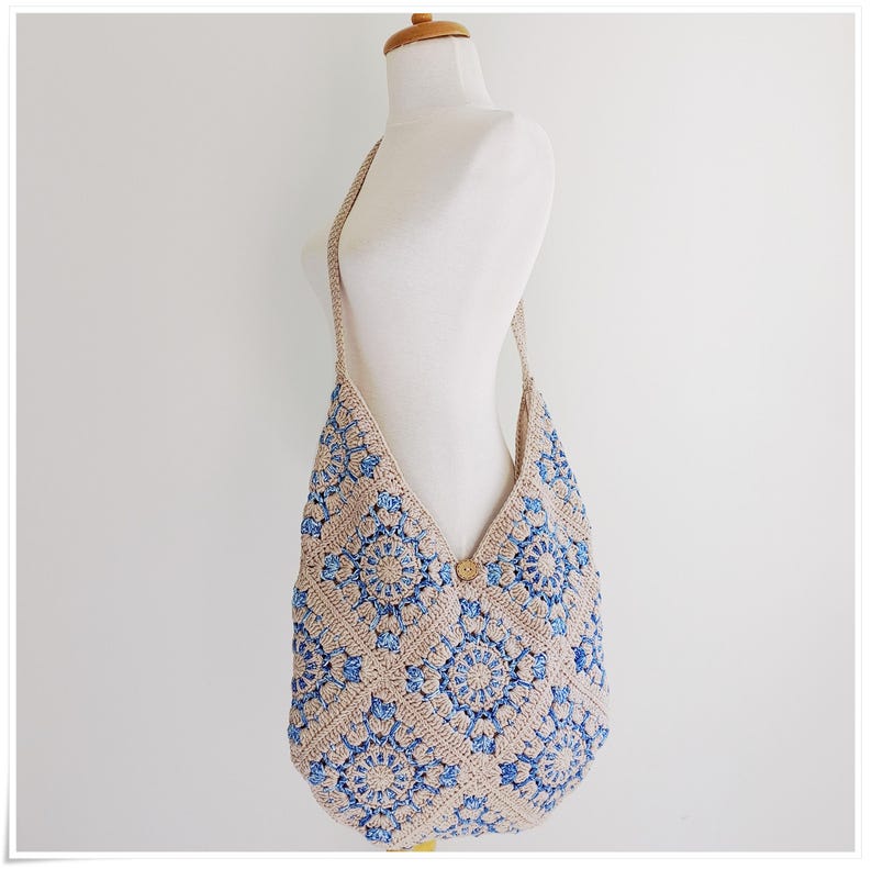 May include: A beige and blue crocheted shoulder bag with a geometric pattern. The bag has a long strap and a wooden button closure.