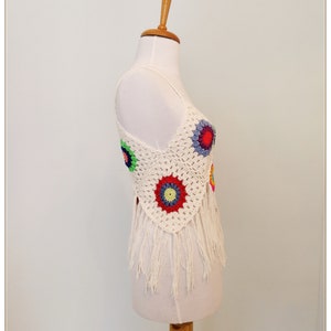 Puede incluir: Top blanco de crochet con dise&ntilde;os circulares coloridos y ribete de flecos. El top se muestra en un maniqu&iacute; blanco.