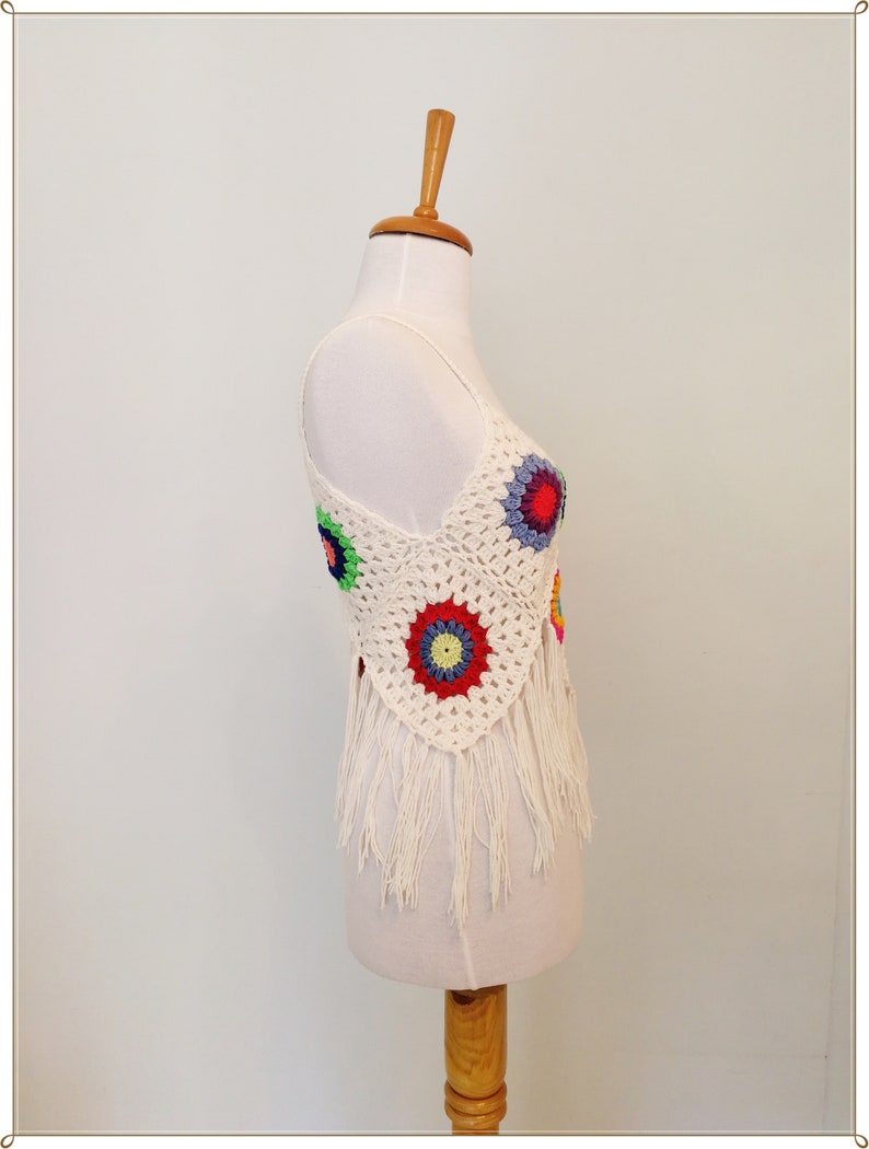 Puede incluir: Top blanco de crochet con dise&ntilde;os circulares coloridos y ribete de flecos. El top se muestra en un maniqu&iacute; blanco.