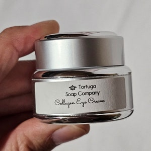 May include: A silver jar with a white label that reads "Tortuga Soap Company Collagen Eye Cream". A small turtle logo is on the label.