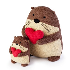 May include: Two plush brown and beige otters holding red heart-shaped stuffed toys. The larger otter is holding a larger heart.