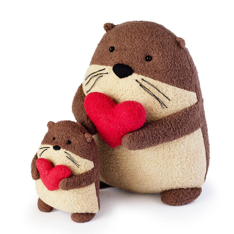 May include: Two plush brown and beige otters holding red heart-shaped stuffed toys. The larger otter is holding a larger heart.