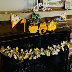 May include: A yellow and black fabric garland with a honeycomb and bee themed paper banner hanging above a fireplace.