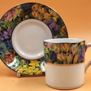May include: A white porcelain teacup and saucer with a floral pattern. The cup and saucer feature a gold trim and a colourful floral design with a variety of flowers, including tulips, daffodils, and irises.