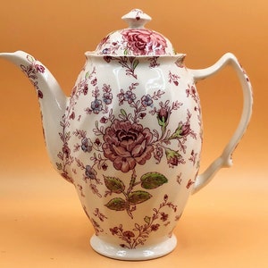May include: A white ceramic teapot with a floral pattern in shades of pink, green, and blue. The teapot has a lid and a handle.