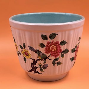 Könnte beinhalten: Weißer Keramiktopf mit hellblauer Glasur innen. Der Topf hat ein Blumenmuster mit rosa, gelben und grünen Blumen und einem Vogel.