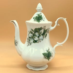 Pode incluir: Cafeteira de porcelana branca com tampa, alça e bico. A cafeteira é decorada com desenhos florais verdes e brancos e detalhes dourados. Uma peça clássica para servir café ou chá.