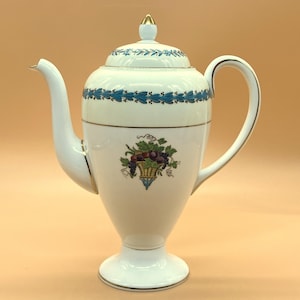 May include: White porcelain coffee pot with a gold trim and a blue and green floral design. The pot has a round body with a spout and a handle.