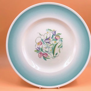 Könnte beinhalten: Ein weißer Keramik-Dinnerteller mit einem blauen und grünen Farbverlauf am Rand. In der Mitte des Tellers befindet sich ein Blumendesign mit rosa, lila und grünen Blumen.