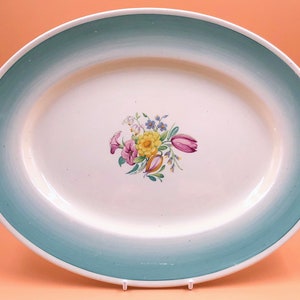 Könnte beinhalten: Eine weiße ovale Servierplatte mit grünem Rand und einem floralen Design in der Mitte. Die Blumen sind rosa, gelb und blau.
