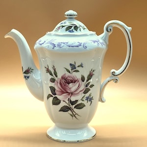 May include: White porcelain teapot with a lid, featuring a large pink rose and floral accents. The handle and spout have gold trim. The teapot is a classic design, suitable for serving tea.