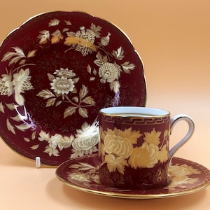 Op de afbeelding: Een rode theekop en schotelset met een gouden bloemenpatroon. De kop en schotel zijn versierd met een delicaat bloemenpatroon in goud op een dieprode achtergrond.