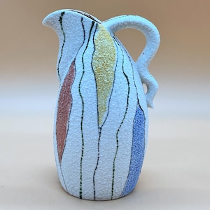 Może przedstawiać: Biały ceramiczny dzban z teksturowaną powierzchnią i zakrzywionym uchwytem. Dzbanek posiada pionowe, faliste paski w kolorze czerwonym, żółtym i niebieskim. Dzbanek ma dzióbek do nalewania.