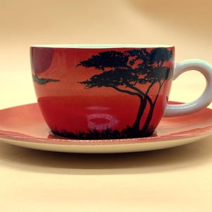 Può includere: Un set da tè in ceramica rossa e bianca con una silhouette nera di un albero su uno sfondo di tramonto.