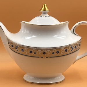 Pode incluir: Bule de porcelana branca com um design floral dourado e azul. A chaleira tem uma tampa com um botão dourado.
