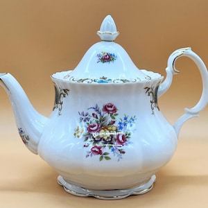 May include: A white porcelain teapot with a floral design. The teapot has a lid with a knob on top and a handle on the side. The floral design features pink, red, yellow, and blue flowers.