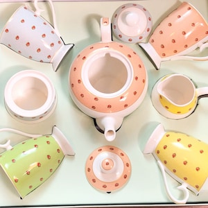 May include: A tea set with a teapot, creamer, sugar bowl, and two cups. The set is decorated with a floral pattern in shades of pink, yellow, and green.