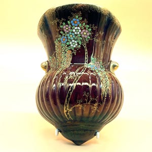 May include: A dark red ceramic wall vase with gold accents and a floral design. The vase has a bulbous body and a flared top.