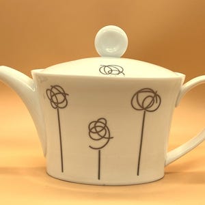 Pode incluir: Bule de chá de cerâmica branca com tampa e design floral abstrato marrom. A chaleira tem um bico e uma alça.