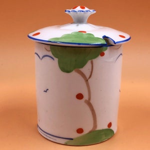 Puede incluir: Jarrón de cerámica blanca con tapa, con un diseño pintado a mano de un árbol verde con bayas rojas y nubes azules. La tapa tiene un pequeño pico y puntos rojos.