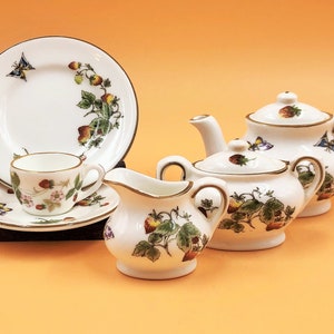 May include: A white porcelain tea set with a strawberry and butterfly design. The set includes a teapot, sugar bowl, creamer, plate, cup, and saucer. The rims are trimmed with gold. The strawberries are red and the butterflies are blue and purple.