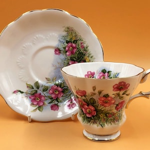 Peut inclure: Une tasse à thé et une soucoupe blanches avec un motif floral de roses roses et de feuilles vertes. L'ensemble est orné d'une bordure dorée.