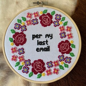 May include: A white embroidery hoop with a floral design and the text "per my last email" in black. The flowers are red, pink, purple, and yellow.