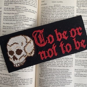 May include: Black bookmark with a cross-stitch skull and the phrase "To be or not to be" in red letters. The bookmark is set against the backdrop of an open book.