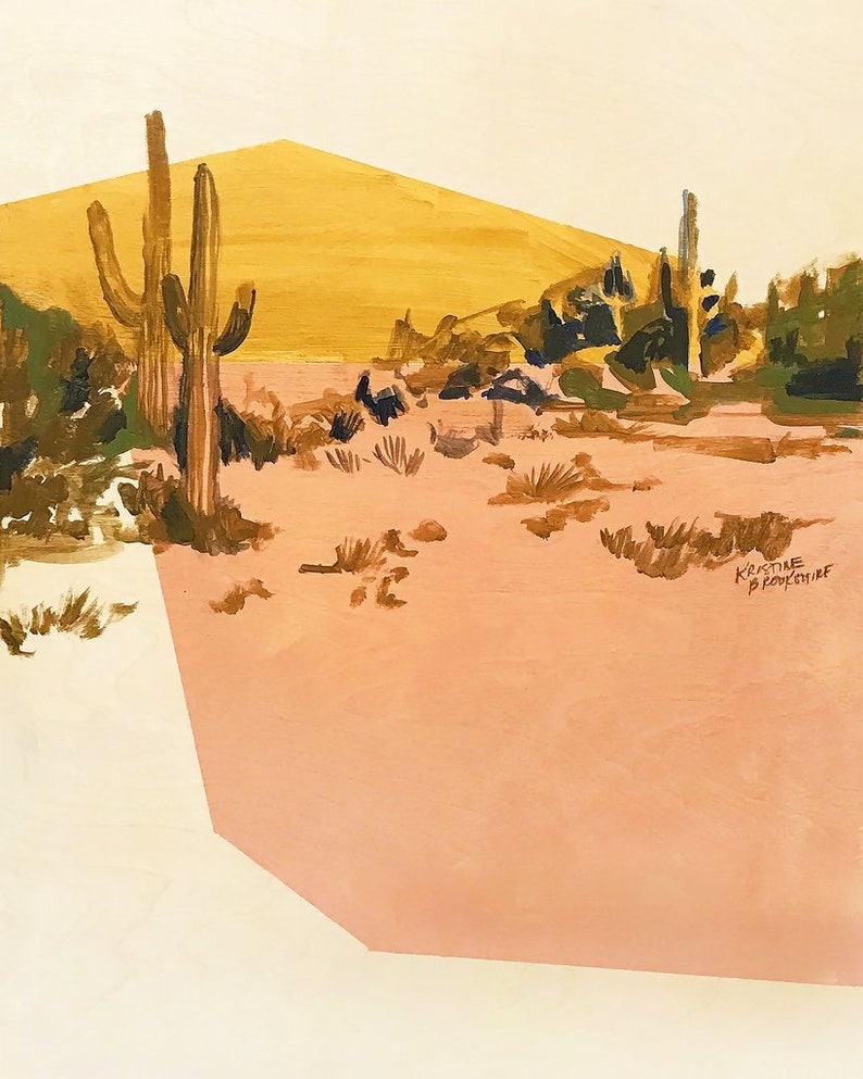 May include: A painting of a desert landscape with a yellow hill in the background and two tall cacti in the foreground. The ground is a light pink color and there are small green bushes scattered throughout the scene. The artist's signature, "Kristine Brochu", is visible in the bottom right corner.