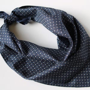 Può includere: Un fazzoletto blu navy con un motivo a pois bianchi. Il fazzoletto è annodato ed è realizzato in un tessuto morbido e fluido. Questo accessorio può essere indossato intorno al collo o sulla testa.