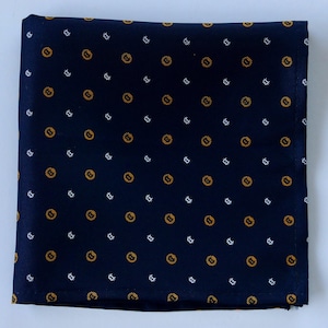 Könnte beinhalten: Marineblaues Einstecktuch mit einem sich wiederholenden Muster aus goldenen und weißen geometrischen Formen. Das Tuch ist sauber gefaltet und zeigt das detaillierte Design. Ein klassisches Accessoire.