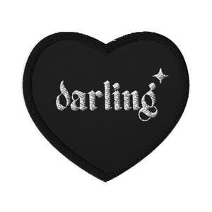 Op de afbeelding: Zwart hartvormig geborduurd embleem met het woord "darling" in witte letters. Naast het woord is een kleine ster geborduurd. De patch heeft een gelaagd ontwerp, met een iets groter zwart hart als basis.