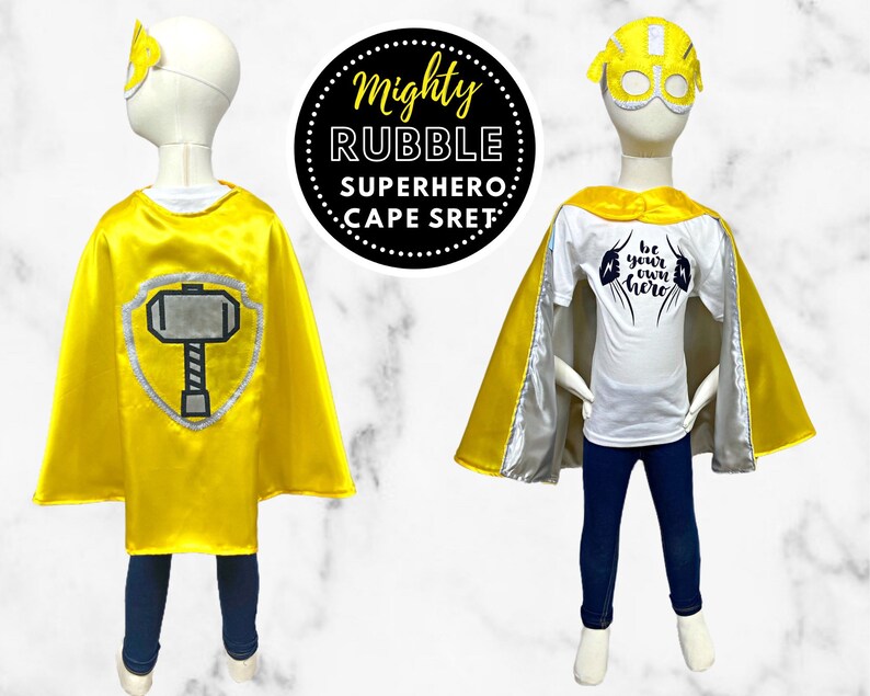 K&ouml;nnte beinhalten: Gelber Superhelden-Umhang mit einem silbernen Hammer-Design auf der R&uuml;ckseite. Der Umhang wird von einer Kinder-Schaufensterpuppe getragen. Das Kind tr&auml;gt auch ein wei&szlig;es T-Shirt mit dem Text "Sei dein eigener Held" in Schwarz.