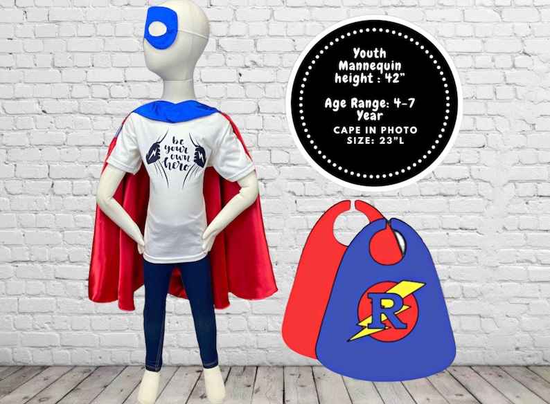 Peut inclure: Un t-shirt blanc avec le texte "Be your own hero" imprim&eacute; dessus. Une cape rouge est drap&eacute; sur les &eacute;paules d'un mannequin portant le t-shirt. Le mannequin porte un jean bleu et un masque pour les yeux bleu. Deux capes sont montr&eacute;es sur le c&ocirc;t&eacute; droit de l'image. Une cape est rouge et l'autre est bleue avec un &eacute;clair jaune et la lettre "R" dans un cercle rouge. Le texte "Youth Mannequin height: 42" Age Range: 4-7 Year CAPE IN PHOTO SIZE: 23"L" est imprim&eacute; en blanc sur un cercle noir.