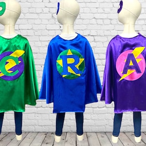 May include: Three superhero capes in different colours with a lightning bolt design. Each cape has a large circle with a letter in the centre: C, R, and A.