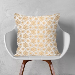 May include: A white throw pillow with a gold geometric pattern. The pillow is sitting on a white chair with wooden legs.