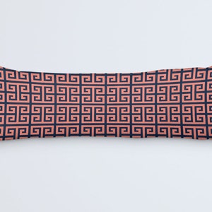 May include: A long, rectangular pillow with a repeating geometric pattern. The pattern features a coral-colored Greek key design on a navy blue background. The pillow is a decorative item, likely for a bed or sofa.