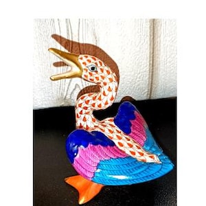 May include: A colorful ceramic bird figurine with an open beak. The bird features orange, white, blue, and pink hues. The beak is gold, and the wings are a mix of blue and pink. The bird's feet are orange.