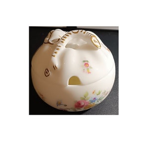 Może przedstawiać: Biała cukiernica z porcelany z kwiatowym wzorem i pozłacaną pokrywką. Pokrywka ma mały otwór do nalewania cukru.